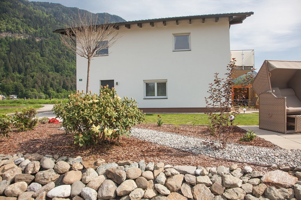 „Hahns Herberge“ – Interiorfotografie Außenansicht; handverlegte Steine mit kleinem Park und Büschen.